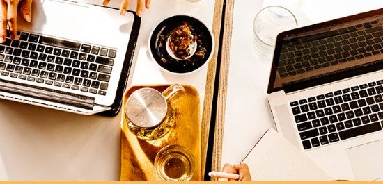 Dois laptops abertos em uma mesa, com chá e doces entre eles