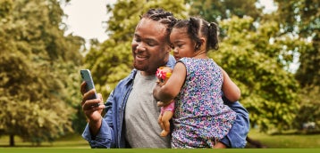 Une personne utilisant son téléphone tout en portant son enfant à l’extérieur.