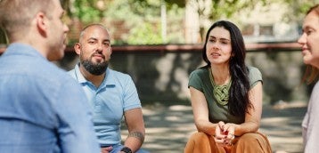 Cuatro personas sentadas al aire libre y conversando